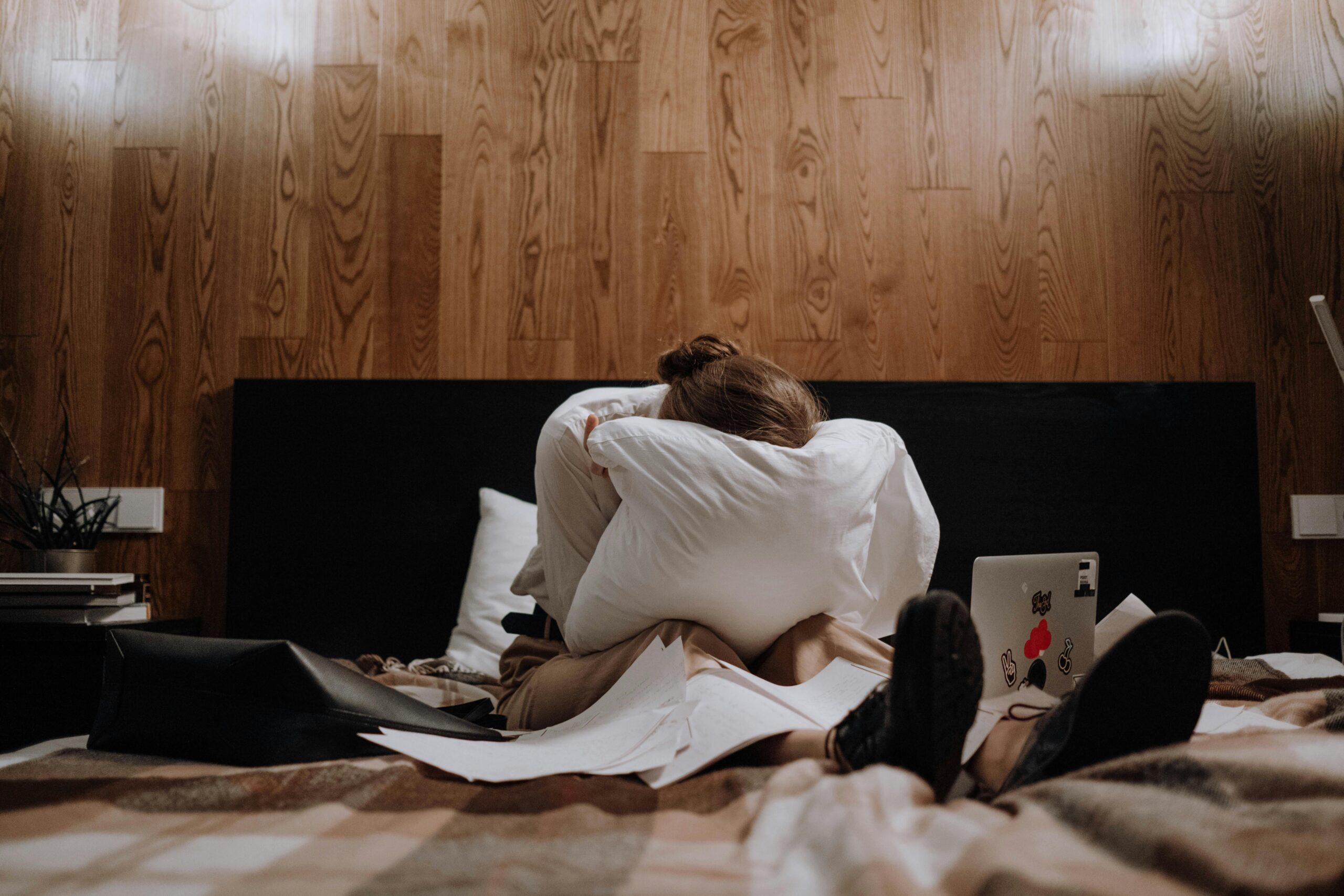Woman relaxing in a cozy bedroom with dim lighting, reading a book as part of a stress-free evening routine for better sleep.