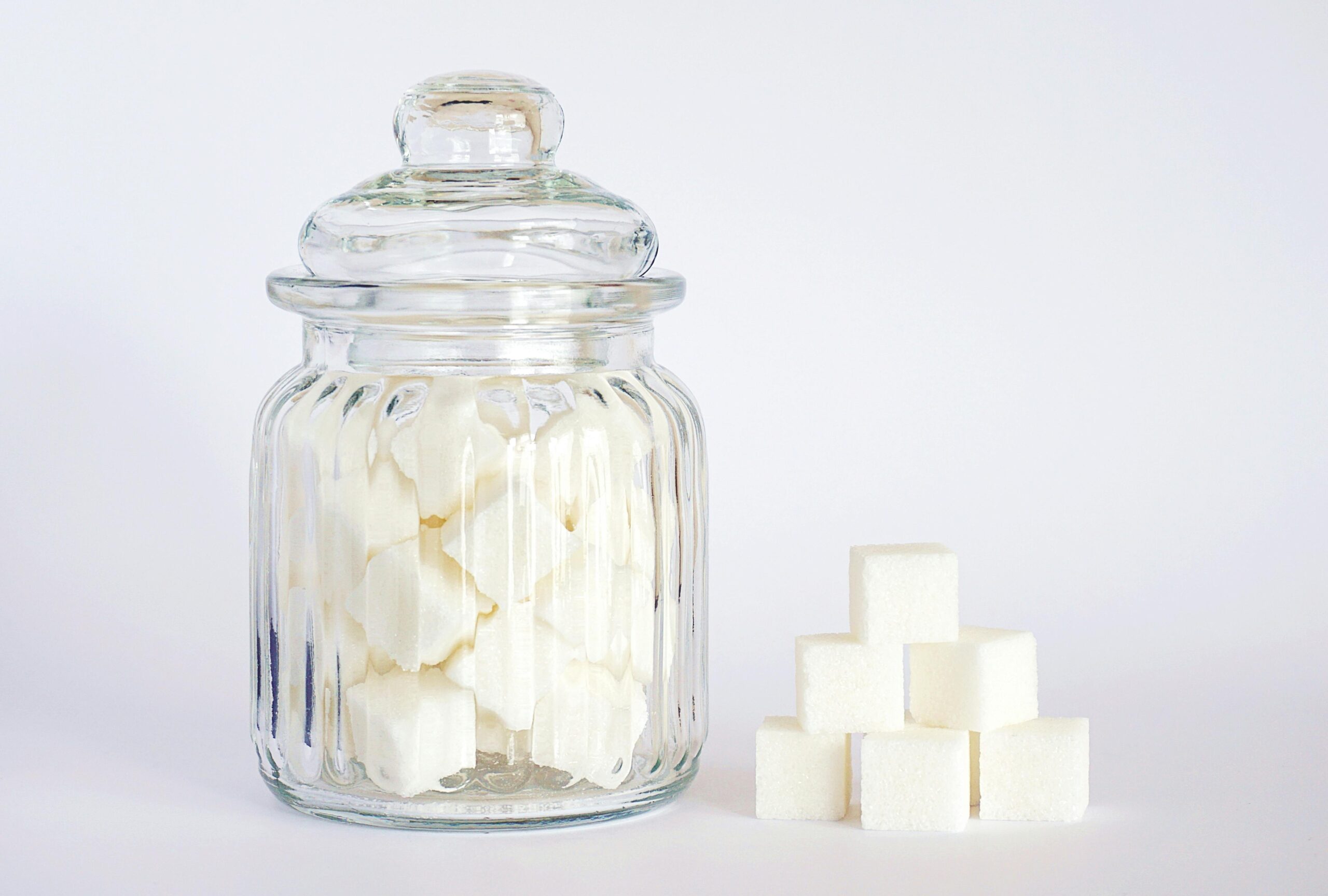 Glass jar filled with white granulated sugar on a kitchen counter, representing added sugar in the diet