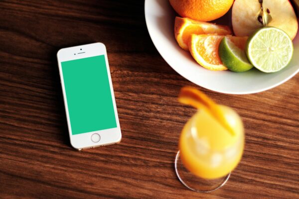 Mockup of a smartphone with fresh citrus fruits and juice on a wooden table.