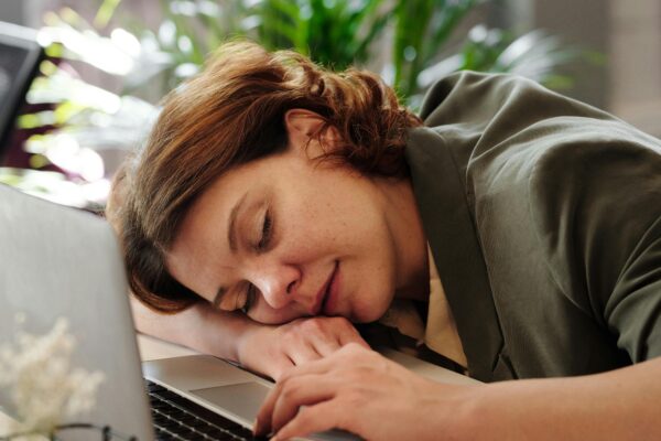 Tired woman in home office resting on laptop, illustrating burnout.