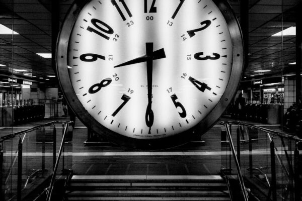 Monochrome image of a large clock at a train station, conveying the passage of time.
