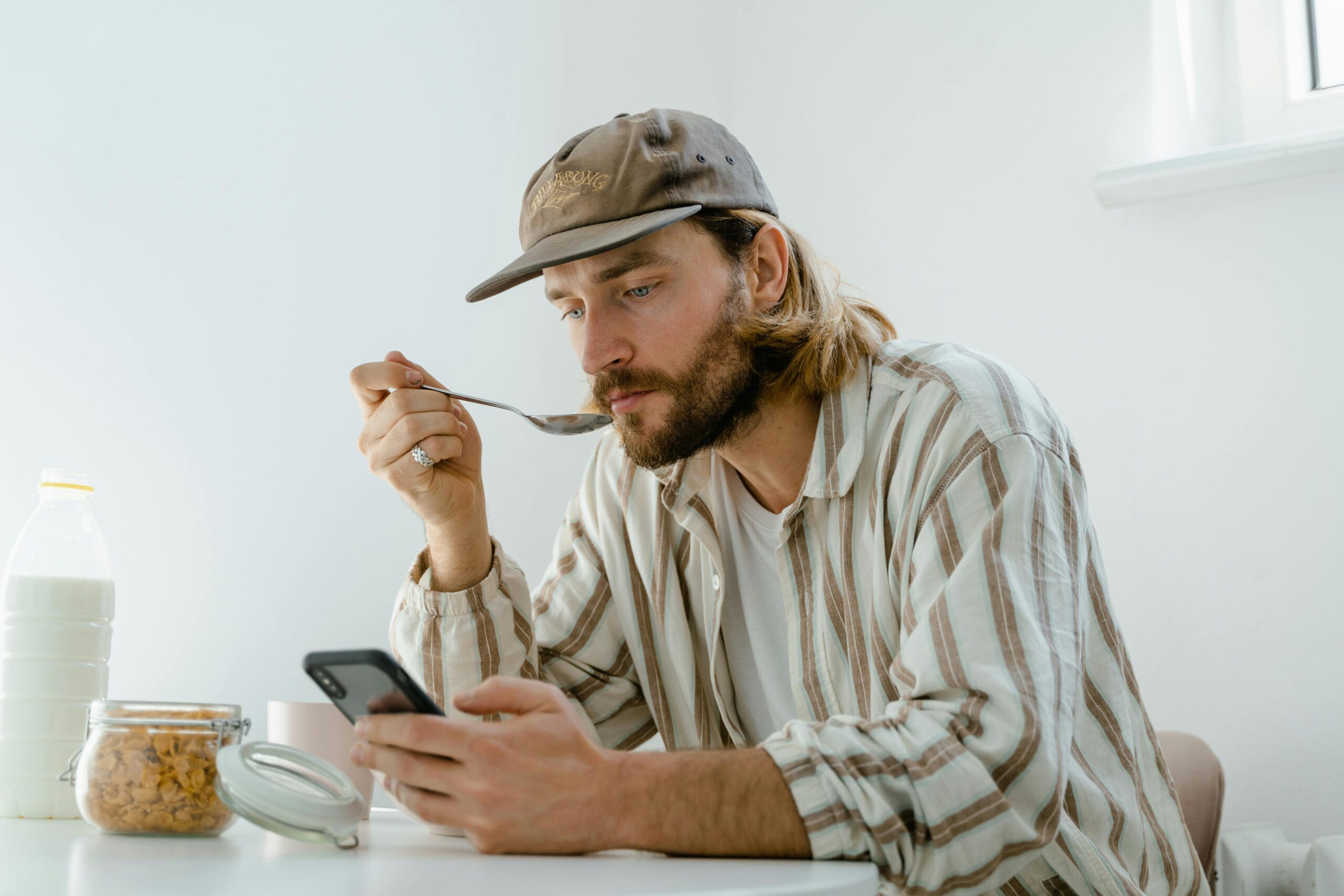 Adult man enjoying breakfast while texting on smartphone, indoors.