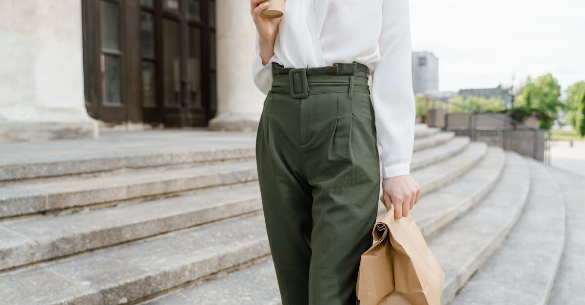 Woman in stylish outfit holding a takeaway coffee and paper bag on outdoor steps.